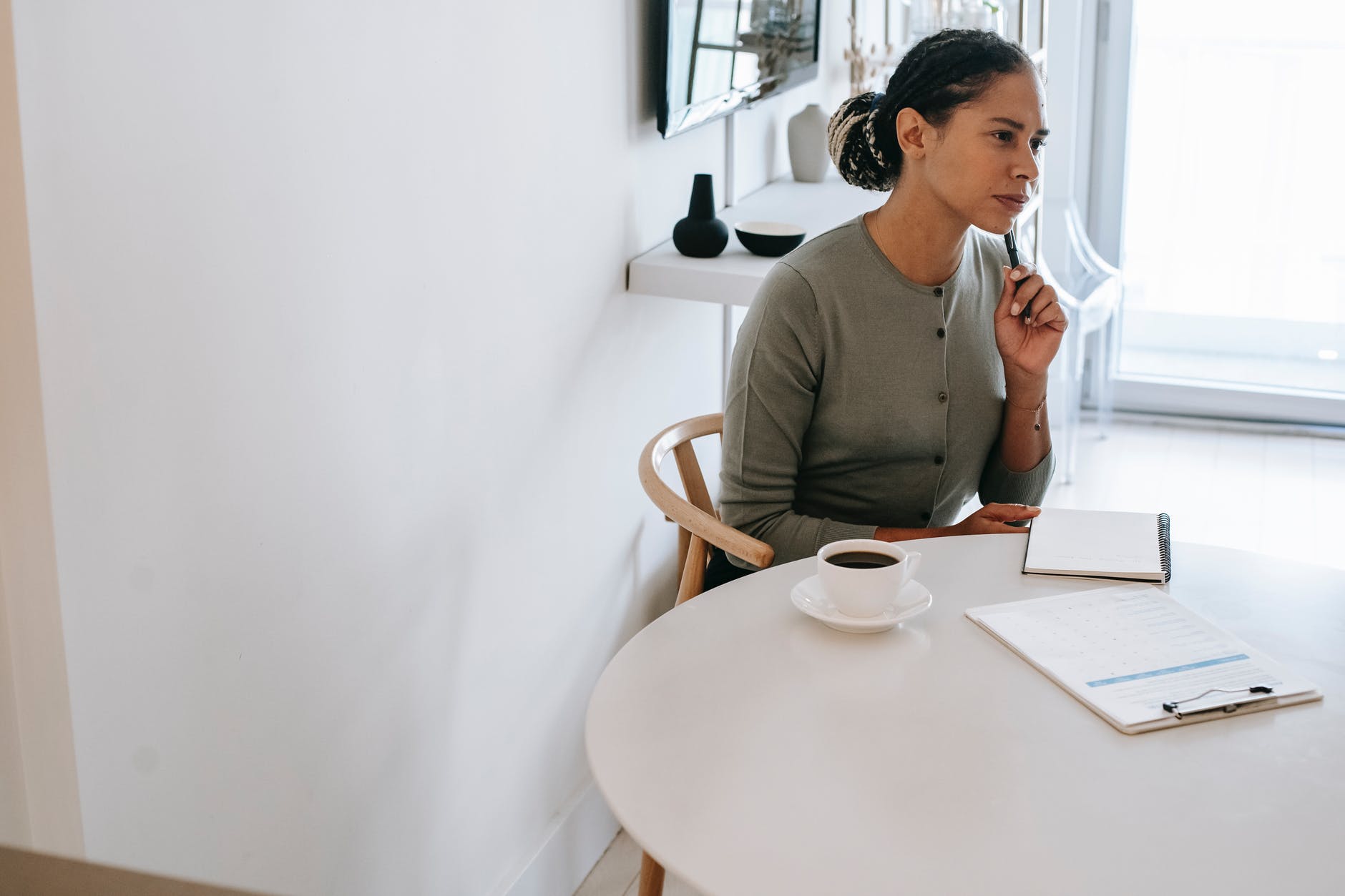 attentive ethnic psychologist sitting at table with pen and clipboard
